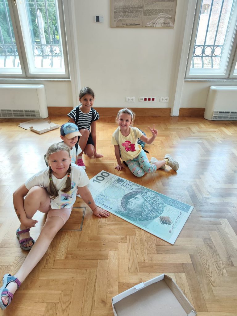 Dzieci pozują do zdjecia z dużym zabawkowym banknotem 100 złotowym